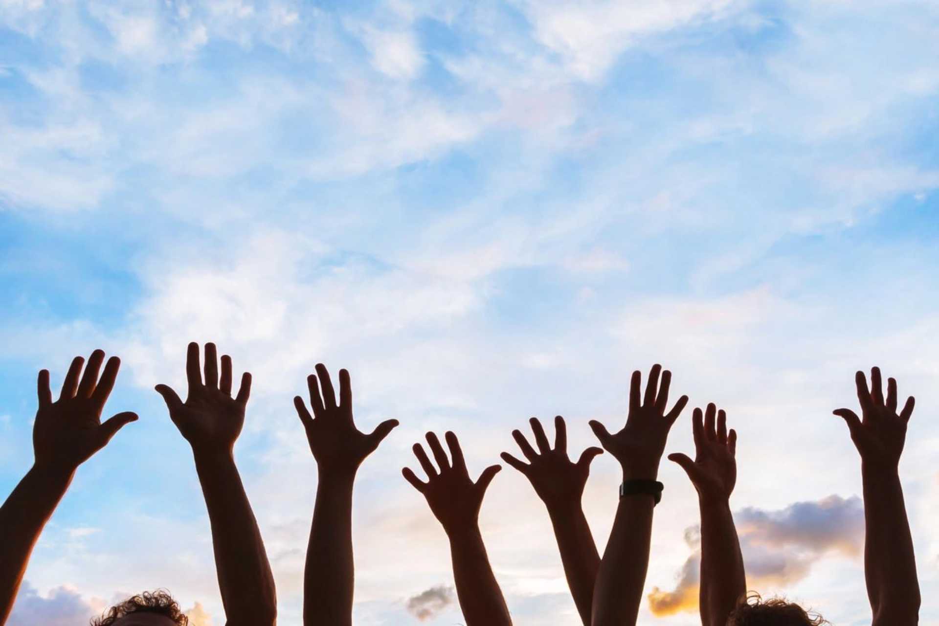 Several pairs of hands raised up against a blue sky with white clouds